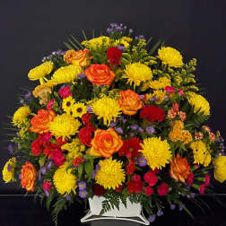 Large mixed flower arrangement in a white vase with yellow, orange, red, and purple blooms