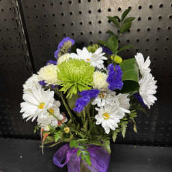 White daisies and purple flowers in a small vase with a purple ribbon