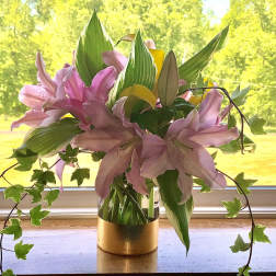 Pink lilies arranged in a gold vase with trailing ivy