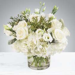 Low white arrangement of roses, hydrangeas, and lisianthus in a clear glass vase