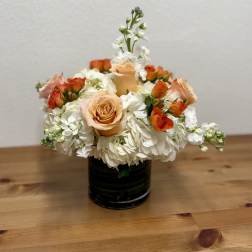 Peach roses and white flowers arranged in a black vase