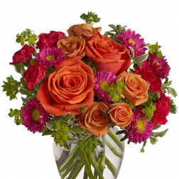 Round arrangement of orange roses and bright pink flowers in a clear glass vase