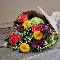 Bouquet of pink roses, yellow daisies, and green hydrangeas wrapped in paper