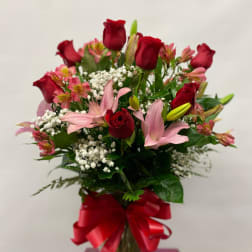 Bouquet of red roses and pink lilies in a glass vase with a red ribbon