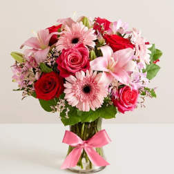 Pink and red mixed flower bouquet in a glass vase with a pink ribbon