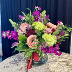 Mixed pink and purple bouquet in a glass vase with a red ribbon