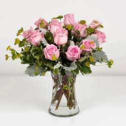 Pink roses arranged in a clear glass vase with greenery
