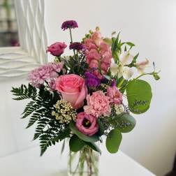 Mixed bouquet of pink and purple flowers with white accents in a clear glass jar vase