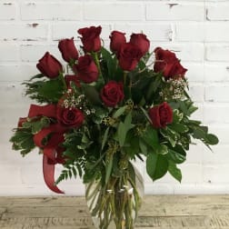 Red roses arranged in a clear glass vase with greenery and a red ribbon