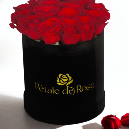 Round black hat box filled with tightly packed red roses with a gold logo on the front.