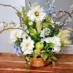 Basket arrangement with white daisies, blue flowers, and green apples