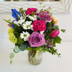 Colorful mixed bouquet with pink rose, carnations, daisies, tulip and iris in a clear glass jar vase
