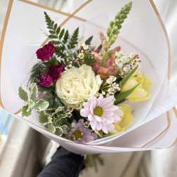 Hand-tied bouquet of mixed pastel flowers wrapped in white paper with a tan border
