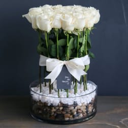 White roses arranged in a glass bowl with a white ribbon
