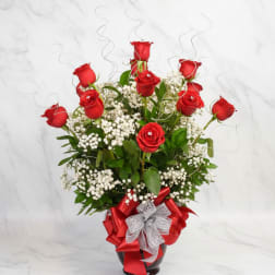 Red roses arranged in a glass vase with white baby's breath and ribbon