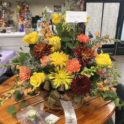 Basket arrangement of yellow roses, orange carnations, and burgundy mums