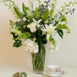 White lilies and roses in a glass vase with kiwi and a teacup