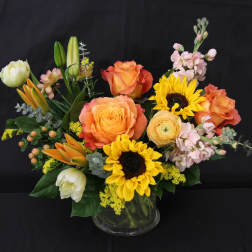 Mixed bouquet with orange roses, sunflowers, and pink blooms in a glass vase