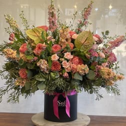 Large pink and peach floral arrangement in a black hatbox with ribbon
