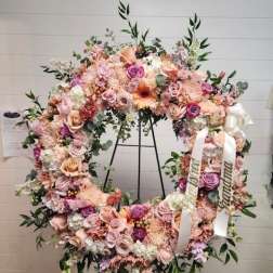 Large pastel floral wreath on a black stand with white ribbons