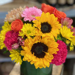 Bright mixed bouquet with sunflowers, roses, gerbera and carnations in a green glass vase