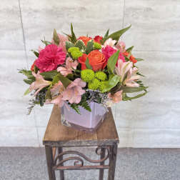 Mixed pink and orange flowers arranged in a square glass vase