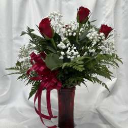 Red roses with baby's breath in a tall red vase with ribbon