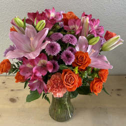 Bouquet of pink lilies, orange roses, and purple mums in a glass vase