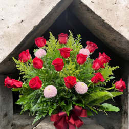 Red roses and pink pompom flowers in a patterned vase with a burgundy ribbon