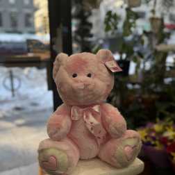 Pink plush teddy bear with a heart ribbon sitting on a pedestal