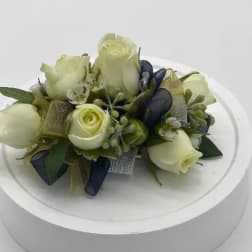 Wrist corsage of ivory roses with navy and gold ribbon on a rhinestone bracelet band