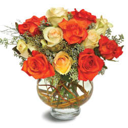 Orange and cream roses arranged in a round clear glass vase with decorative twigs in the water