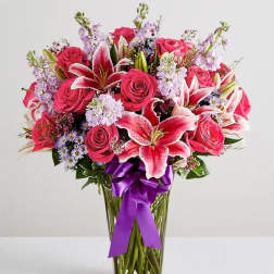 Bouquet of pink roses and lilies in a clear glass vase with a purple ribbon