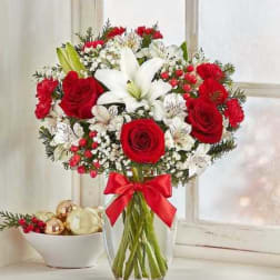 Red roses and white lilies in a clear glass vase with a red ribbon