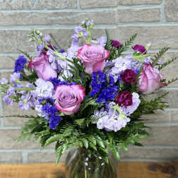 Mixed bouquet of pink roses, purple blooms, and lavender flowers in a clear glass vase