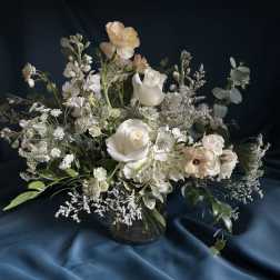 Asymmetrical arrangement of white and cream flowers in a clear glass vase on a dark fabric backdrop