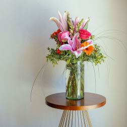 Tall bouquet of pink lilies and orange flowers in a glass vase