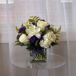 White roses and lilies in a glass vase with purple accents