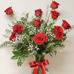Red roses arranged in a clear glass vase with a red ribbon.