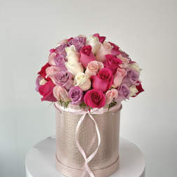 Pink and lavender roses arranged in a round hatbox with a ribbon