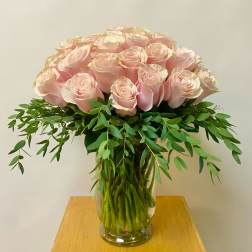 Pink roses arranged in a clear glass vase with trailing greenery