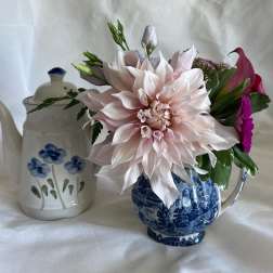 Pastel dahlia and mixed pink flowers arranged in a blue teacup beside a white floral teapot.