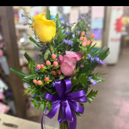 Bouquet of yellow and pink roses in a glass vase with a purple ribbon