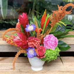 Colorful tropical bouquet in a white vase with pink, orange, purple, and green blooms