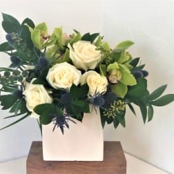 White roses and green orchids in a white square vase