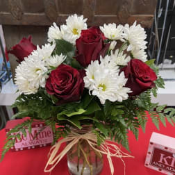 Red roses and white daisies in a glass vase with a raffia bow