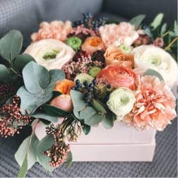 Peach and white flowers arranged in a white box with eucalyptus