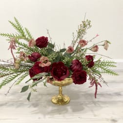 Deep red floral arrangement in a gold pedestal bowl