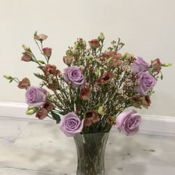 Lavender roses and small pink blooms in a clear glass vase