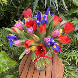 Colorful tulip bouquet in a glass vase with a red ribbon